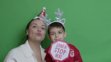 Anne ve oğlu Noel Baba 'yı Noel Baba Dur tabelası ve baş dekorasyonuyla evlerine davet etti. Yavaş çekim yakın çekim, yeşil arka planda izole. Yüksek kalite 4k görüntü
