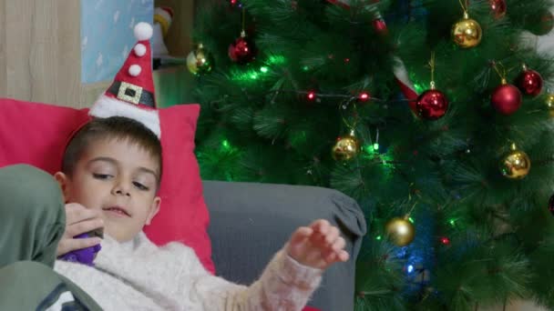 Χαριτωμένο Αγόρι Ξαπλωμένο Στον Καναπέ Σηκώνεται Και Κοιτάζει Χριστουγεννιάτικο Δέντρο — Αρχείο Βίντεο