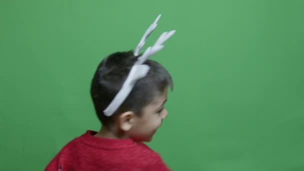 可爱的学龄前男孩 穿着红色毛衣 鹿角旋转和眨眼 在绿色的背景下被隔离 慢动作 高质量的4K镜头 — 图库视频影像
