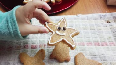Çocuk, beyaz kremayla süslenmiş yıldız şeklindeki zencefilli kurabiyeleri topluyor ve farklı şekilli kurabiyelerle birlikte kırmızı tabağa koyuyor. Yüksek kalite 4k görüntü