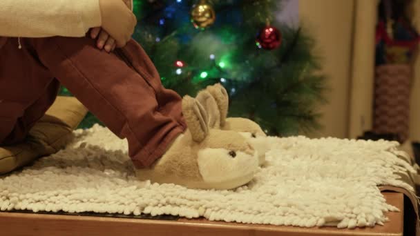 Noel Ağacının Yanında Oturan Sevimli Çocuk Yeni Tavşan Terlikleriyle Oynuyor — Stok video