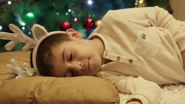 クリスマスツリーの近くで眠っているかわいい少年が目を開けて立ち上がります 高品質の4K映像 — ストック動画