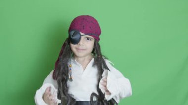 Kostüm partisi. Yeşil arka planda poz veren peirate kostümlü bir çocuk. Kopyalama uzayı ile yavaş çekim. Yüksek kalite 4k görüntü