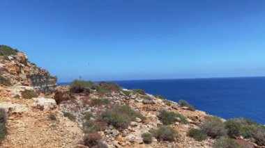 Etrafta martıların uçtuğu ve adaya doğru giden teknelerin olduğu güzel Comino Adası kayalıkları. Engebeli arazide yürüyüş yolu. Yüksek kalite 4k görüntü