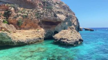 Turkuaz deniz suyu ve arka planda küçük doğal kemerli kireçtaşı kayalıkları. Ay plajından Comino Adası manzarası. Yüksek kalite 4k görüntü