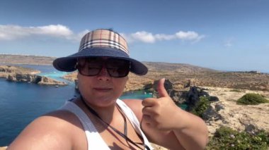 Güneş gözlüklü ve şapkalı kadın turistler Coino Adası 'nın kayalıklarında selfie çekerken başparmaklarını gösteriyorlar. Yüksek kalite 4k görüntü