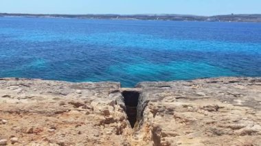 Denize doğru giden kayalıklarda kesikler, arkada Comino Adası ve Malta. Yüksek kalite 4k görüntü