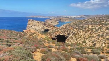 Etrafta martıların uçtuğu ve adaya doğru giden teknelerin olduğu güzel Comino Adası kayalıkları. Engebeli arazide yürüyüş yolu. Yüksek kalite 4k görüntü