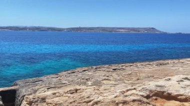 Denize doğru giden kayalıklarda kesikler, arkada Comino Adası ve Malta. Yüksek kalite 4k görüntü