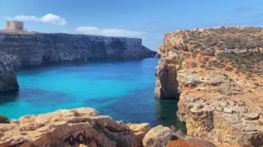 Güzel Comino deniz mağaraları ve doğal kemerler. Kristal berrak Akdeniz 'de bir tekne. Santa Marija kulesinin yakınındaki kayalıklardan görüldü. Yüksek kalite 4k görüntü