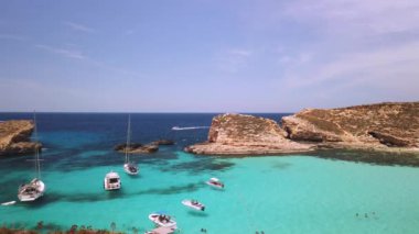 Comino, Malta 29.05.2024 - Mavi Göl 'ün güzel kristal berrak turkuaz suyu. Tekneler yüzüyor, turistler yüzüyor. Arka plandaki Cominotto adasında. Yüksek kalite 4k görüntü