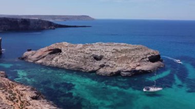 Kristal berrak turkuaz deniz suyunda yüzen tekneler. Mavi Göl, Comino, Malta Adaları. Havadan statik çekim. Yüksek kalite 4k görüntü