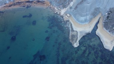 Tat-Tonn or Spritzing rock, snorkeling point between Qarraba Bay and TaBabu Cove, Ghajn Tuffieha, Mgar, Malta. Aerial view of the emerald sea and rocky coast in early morning still in the shade of clipart