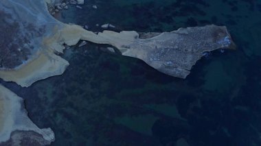 Tat-Tonn ya da Spritzing kayası, Qarraba Körfezi ile TaBabu Koyu, Ghajn Tuffieha, Mgar, Malta arasında şnorkelle yüzme noktası. Sabahın erken saatlerinde zümrüt deniz ve kayalık kıyı manzarası hâlâ gölgede.