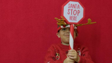 Sevgili boynuzları olan tatlı çocuk Noel Baba dur tabelasını burada tutuyor. Noel arkaplanı. Yüksek kalite fotoğraf