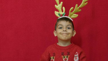 Noel tatili. Kırmızı arka planda izole edilmiş geyik boynuzlarını ayarlayan tatlı çocuk. Yüksek kalite fotoğraf