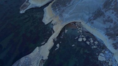 Tat-Tonn or Spritzing rock, snorkeling point between Qarraba Bay and TaBabu Cove, Ghajn Tuffieha, Mgar, Malta. Aerial view of the emerald sea and rocky coast in early morning still in the shade of clipart