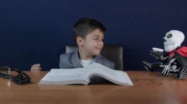 Finansal eğitim. Takım elbiseli bir çocuk kitap okuyor, iskelet para kutusuna bakıyor ve yeşil emoji atıyor. Yüksek kalite 4k görüntü