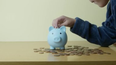 Çocuk tasarrufu konsepti. Bir çocuk mavi kumbarasına bozuk para koyar ve onu öper. Yüksek kalite 4k görüntü