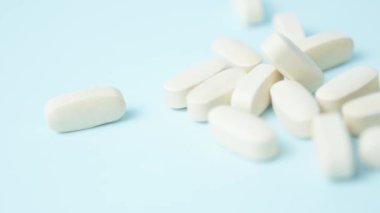 Açık mavi arka planda beyaz haplar, yumuşak odak, makro, sağa doğru dönen. Yüksek kalite 4k görüntü