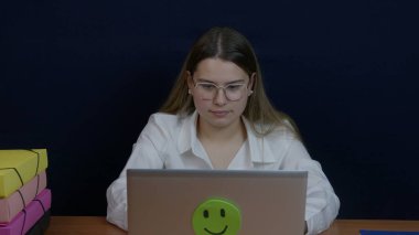 Profesyonel bir kadın masa başında oturuyor. Belgeler, dizüstü bilgisayarlar ve dosyalarla çalışıyor. Sahne üretkenliği aktarıyor ve modern ofis ortamında odaklanıyor.