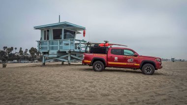 Santa Monica Plajı 'nda bulutlu bir günde bir cankurtaran kulesi ve kırmızı bir pikap görüyorum.
