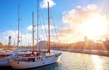 Barselona İspanya. Şık yatlar ve teknelerle gün batımında iniş yapmak. Işın güneşinde şehir manzarası.