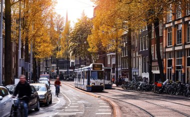 Amsterdam, Hollanda. Sokak manzarası, modern tramvay, güneşli bir sonbahar akşamında hareket eden toplu taşıma. Bisiklet yolda.