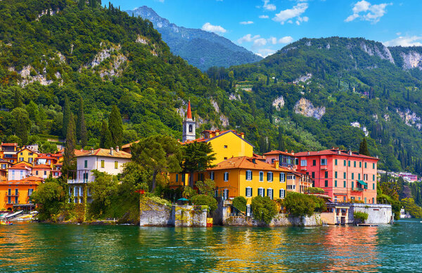 Varenna, Italy. Picturesque town at lake Como. Colourful motley Mediterranean houses stone beach coastline among green trees. Popular health resort and touristic location. Summer day landscape