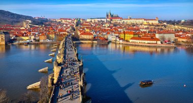 Prag, Çek Cumhuriyeti. Charles Köprüsü, Prag Kalesi ve Vltava Nehri 'nin panoramik manzarası. Eski kasaba evleriyle manzaralı, kırmızı tegıl çatıları olan bir tekne.
