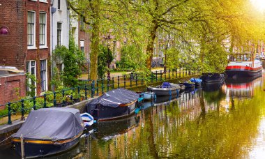 Hollanda Amsterdam 'da. Amstel nehrinin manzarasına bak. Geleneksel evler bankada ve tekneler su kanalında. Manzaralı şehir manzarası. Bahar günü.