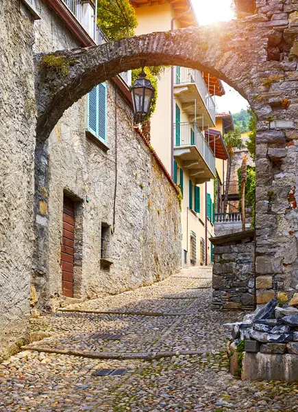 Varenna, İtalya. Lombardy bölgesindeki Como Gölü 'ndeki eski Akdeniz kasabasının binaları arasında taş yay ve Vintage lamba bulunan antika dar bir sokak. Güneşli yaz günü.