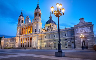 Madrid, İspanya. Santa Maria la Real de la Almudena Katedrali Plaza de la Armeria 'da. Günbatımı güneşi, çiçekler ve yeşil çalılarla ünlü bir yer. Işıklı sokak lambaları ve mavi gökyüzü.