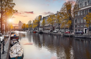 Amsterdam, Hollanda. Amstel nehrindeki ünlü evlerin panoraması, tekneli su kanalları. Eski Avrupa şehrinde popüler bir dönüm noktası ve seyahat noktası. Akşam batımı manzarası.