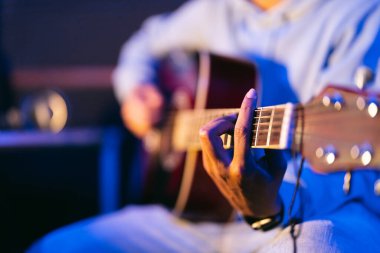 Siyah arka planda akustik gitar çalan gözlüklü genç bir Afrikalı müzisyen