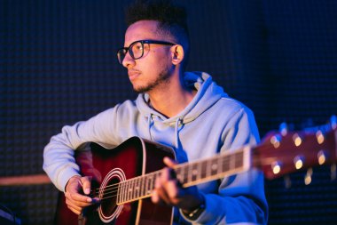 Siyah arka planda akustik gitar çalan gözlüklü genç bir Afrikalı müzisyen