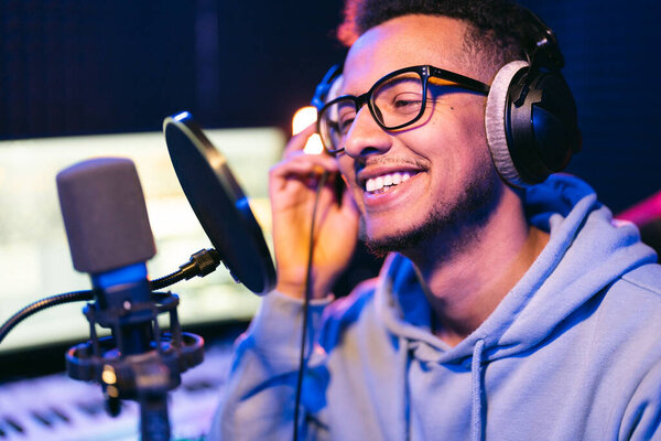 Male vocal artist, singer, podcaster with curly hair, headphones in sound studio recording new melody or album.