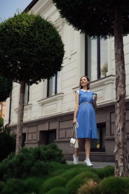 Mavi elbiseli güzel hamile bir kadın şehir sokaklarında yürüyor ve içki içiyor..