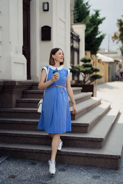 身穿蓝色衣服的漂亮的年轻孕妇穿过城市街道 一边喝酒一边喝 — 图库照片