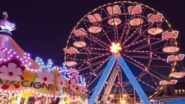 Rovigo, İtalya 25 Ekim 2022: Funfair dönme dolabı gece. Gece lunaparkta dönme dolap ve lunaparkta hız treni hareket ediyor.