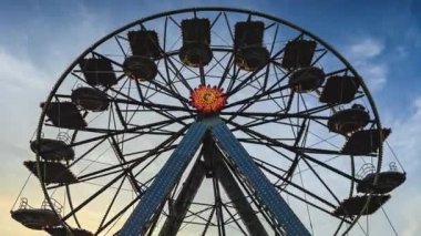 Gün batımında lunapark dönme dolabı. Birçok kulübesi olan dönme dolabın silueti gün batımında eğlence parkında sıcak turuncu gökyüzüne doğru dönüyor.