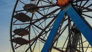 Gün batımında lunapark dönme dolabı. Birçok kulübesi olan dönme dolabın silueti gün batımında eğlence parkında sıcak turuncu gökyüzüne doğru dönüyor.