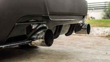 Yeni lüks bir arabanın egzoz sisteminin alt görüntüsü. Panoramik manzara. Zararlı maddeleri motor egzozundan temizlemek ve araç gürültüsünü azaltmak için çift egzoz borusunu kapatın..