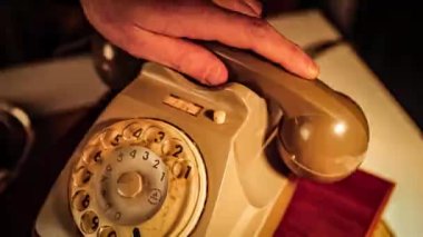 The hand of a man picks up the receiver of a vintage telephone and puts it back