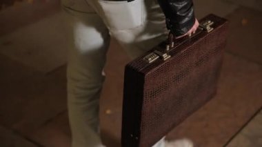 Man in a black jacket walks on road with a briefcase full of cash won at casino
