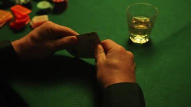 Poker cards in hands with whiskey glass and poker chips scattered on green table