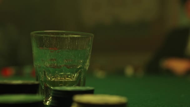 ポーカーチップに囲まれたポーカーテーブルの上に置かれたガラスにウイスキーを注ぐ — ストック動画