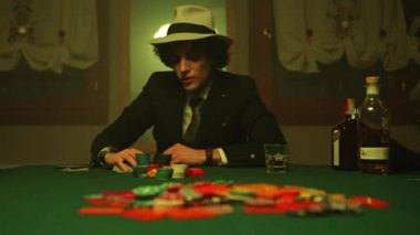 New York, United States 17 January 2023: A drunk poker player in a cow-boy hat sipping whiskey while checking his cards placed in front of him on the table. He adds all his poker chips to the pile scattered on the table signalling an all-in bet.