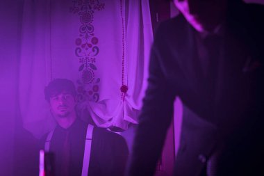 A mobster dressed in a suit and a cowboy hat is sitting in a dimly lit room. He has an intense and serious expression on his face, conveying a sense of power and danger.