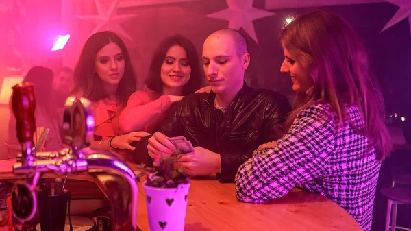 A man with a stack of cash and surrounded by women. Throws away some of the cash on the table. He is likely gambling. Suggests a concept of luxurious nightlife, gambling, and entertainment.